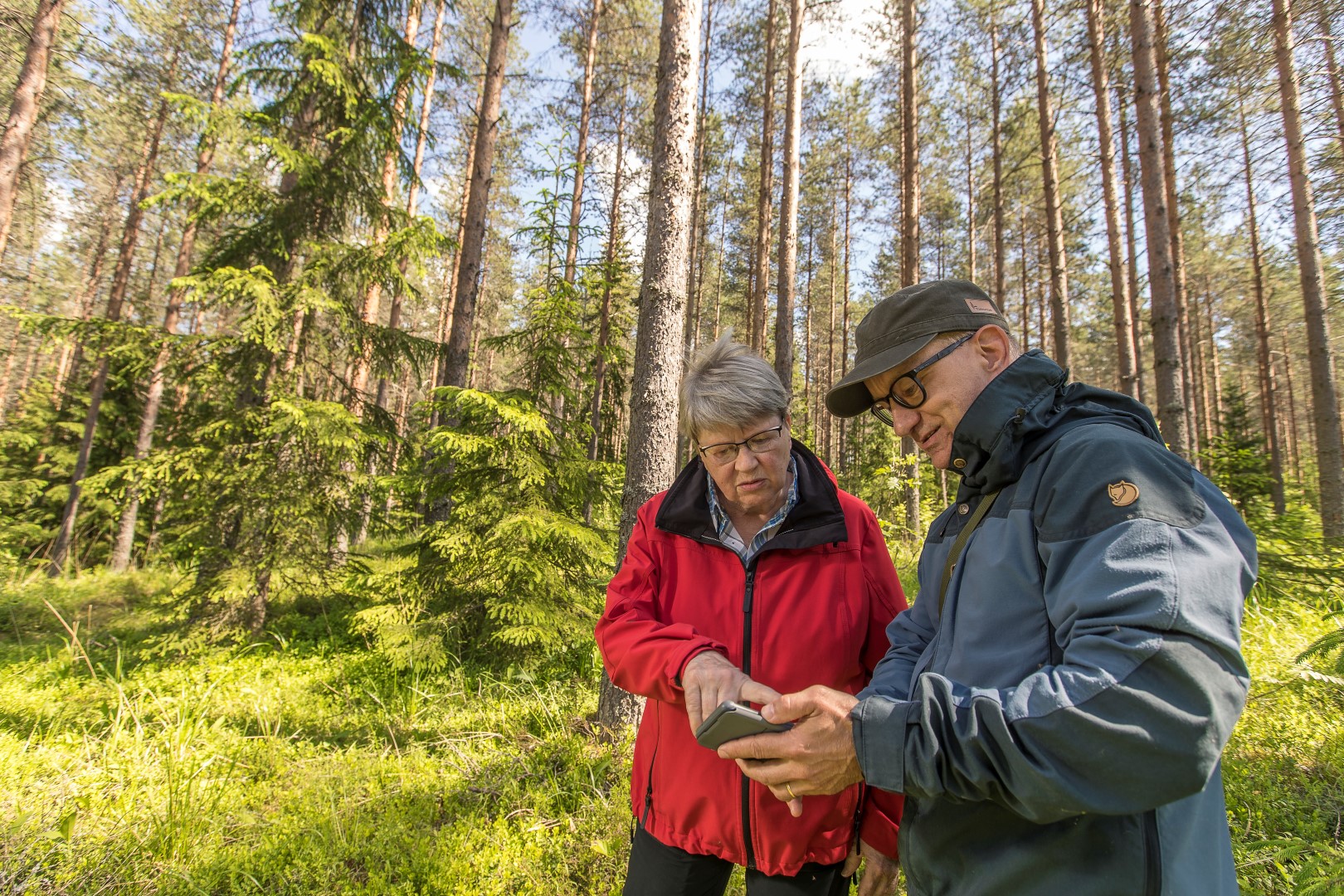 Mies ja nainen metsässä. Miehellä on kädessään puhelin, jota hän näyttää naiselle.