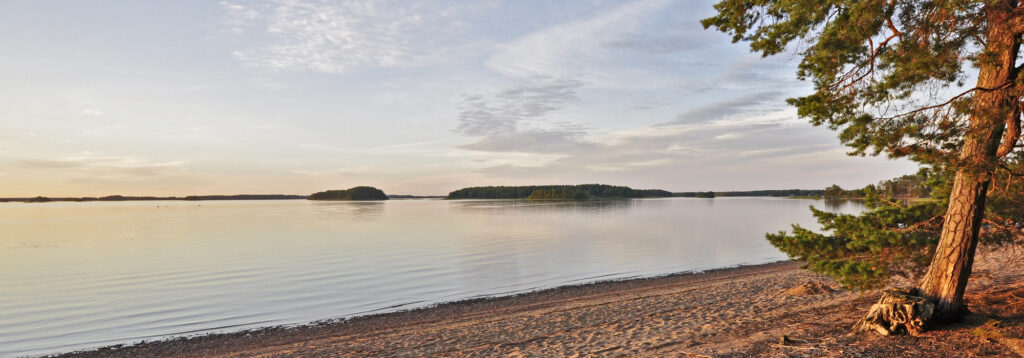 Hiekkaranta ja tyyni järvi ilta-auringossa.