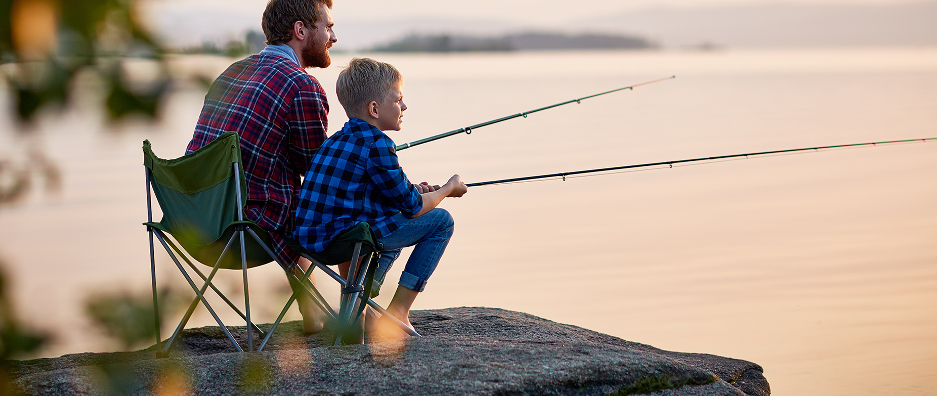 Mies ja poika kalastamassa rantakalliolla ilta-auringossa.